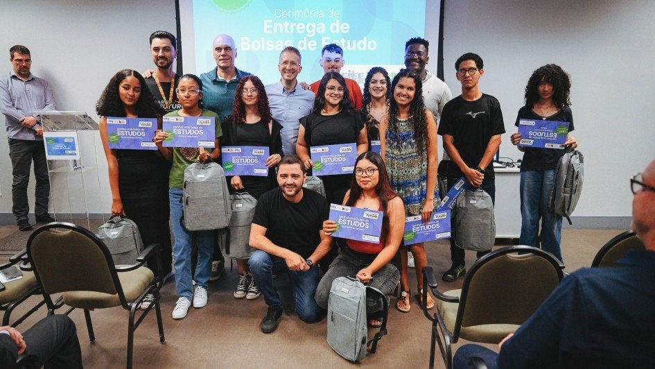 Beto Fantinel, Gabriel Souza e os onze bolsistas posam para a foto em frente a um telão